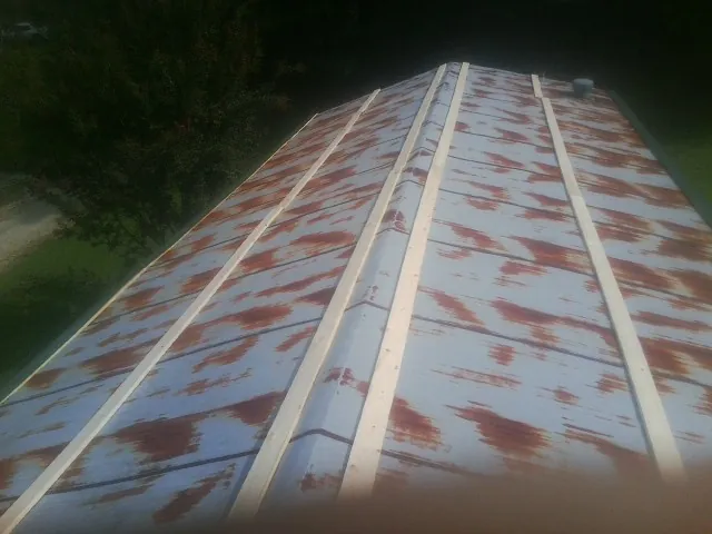 Rusted metal roof panels with new wood purlins before replacement in Sibley
