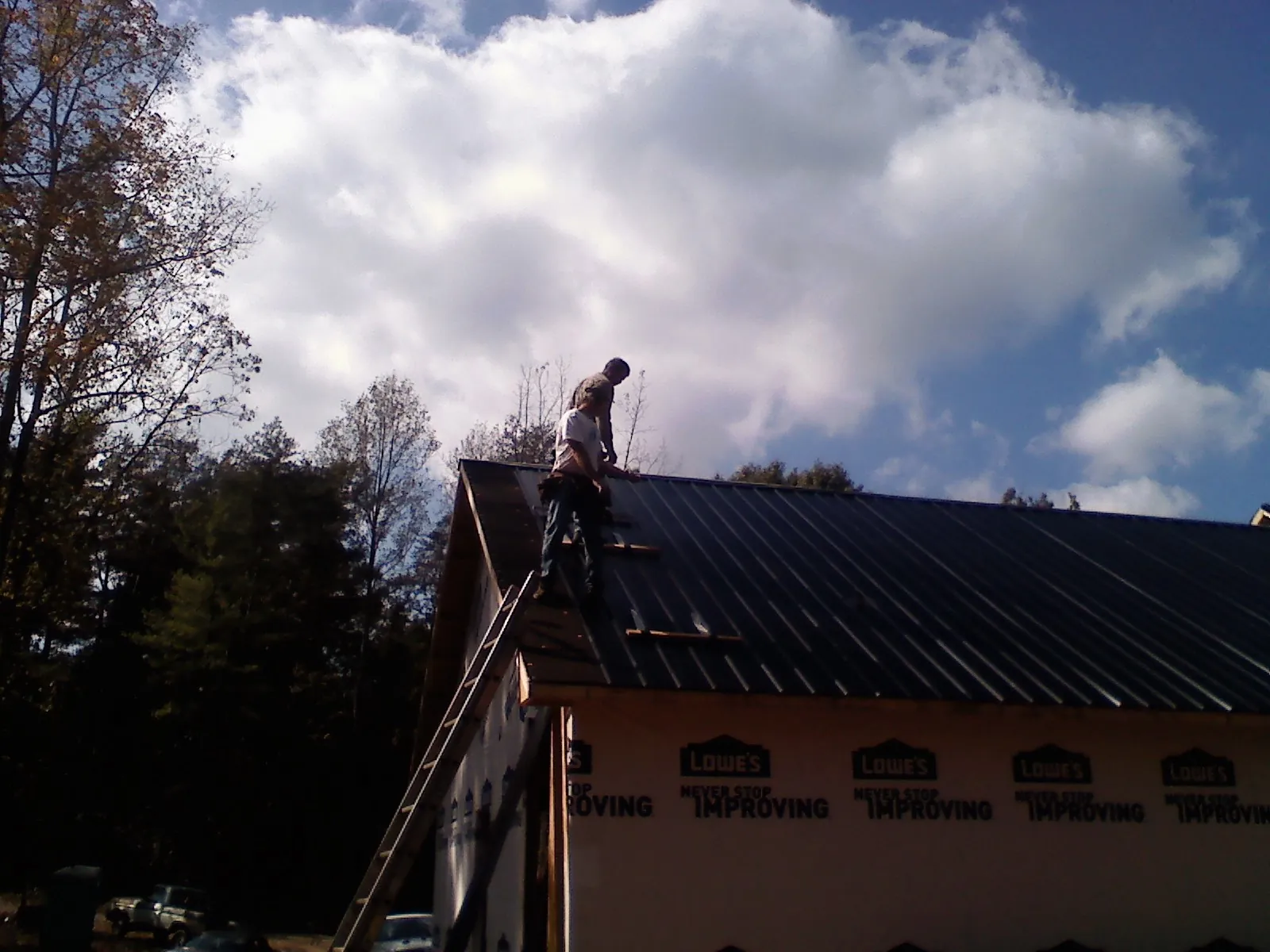 Roofer fastening dark metal panels high against a cloudy sky, from a Roof Inspection job in Sibley