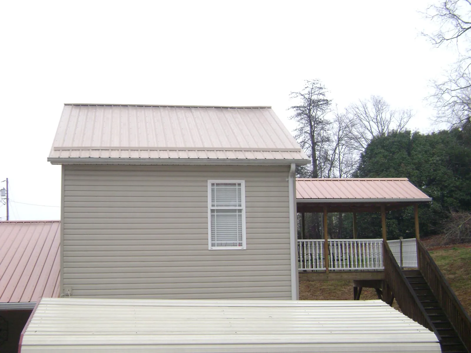 Tan metal roofs on a two story addition and attached porch, from a Roof Replacement job in Sibley